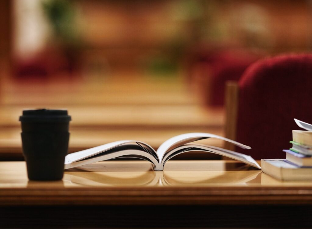 An open book and coffee cup on a table.