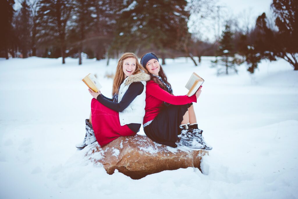 Two girls reading together on a snowy rock